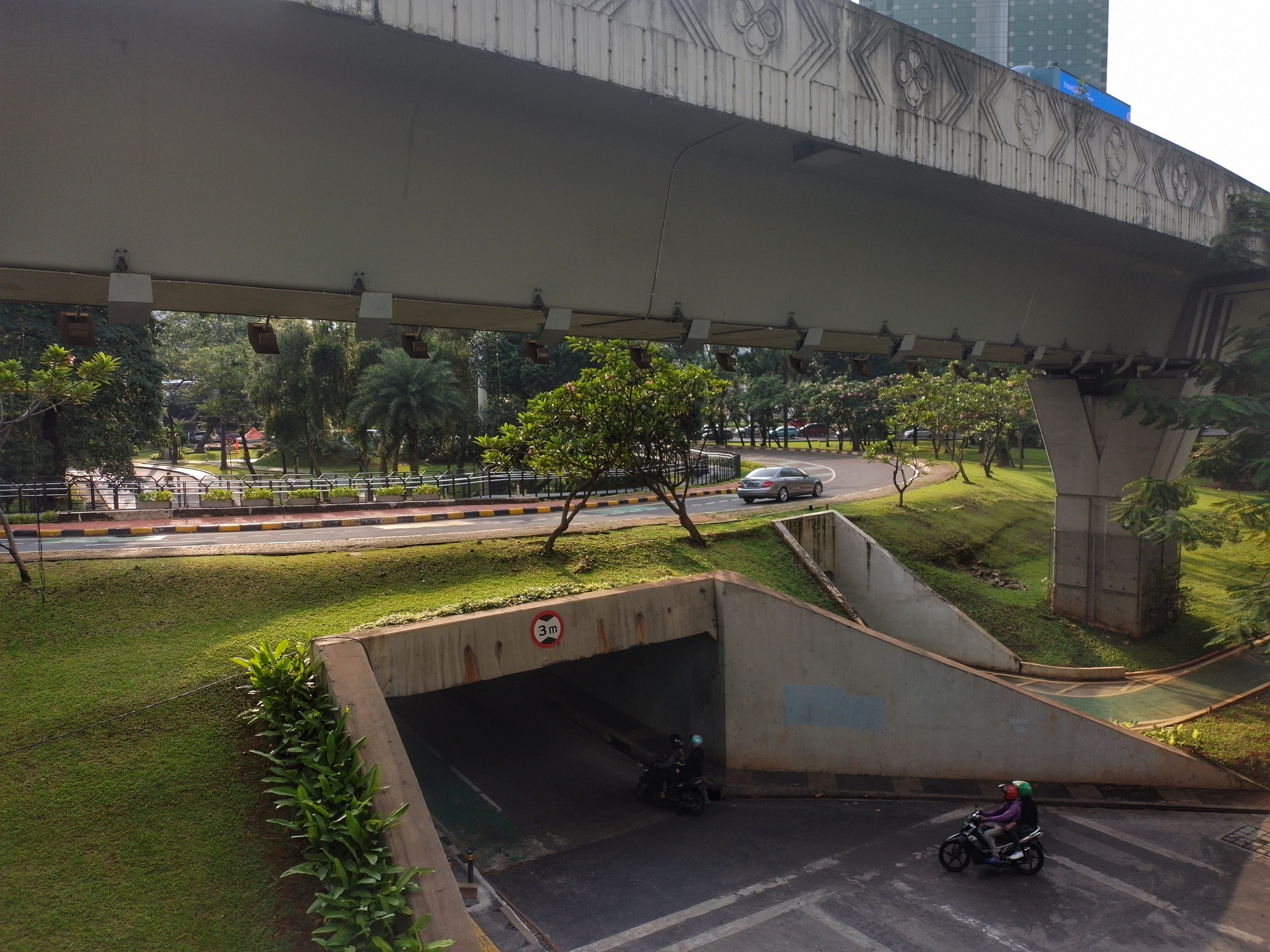 Motorbike riders in helmets ride out of an underpass beneath a concrete flyover in Jakarta