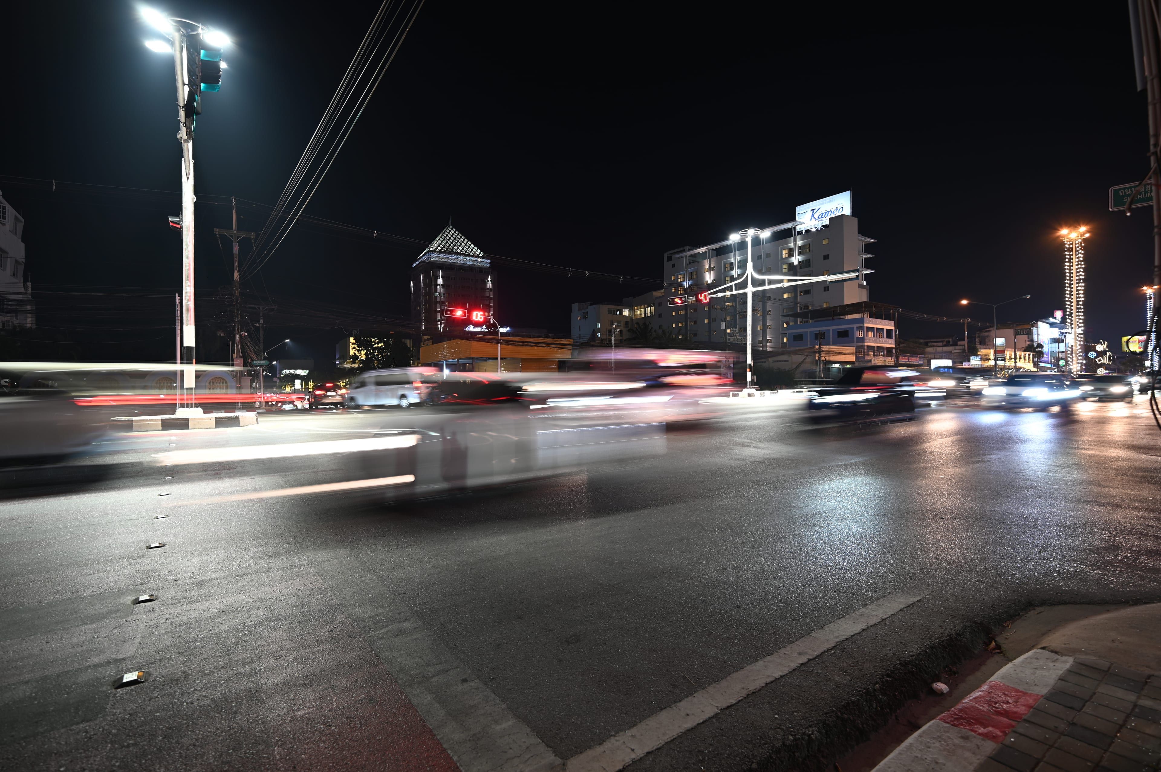 Blurred cars leave light trails across a wide city intersection at night under tall streetlights