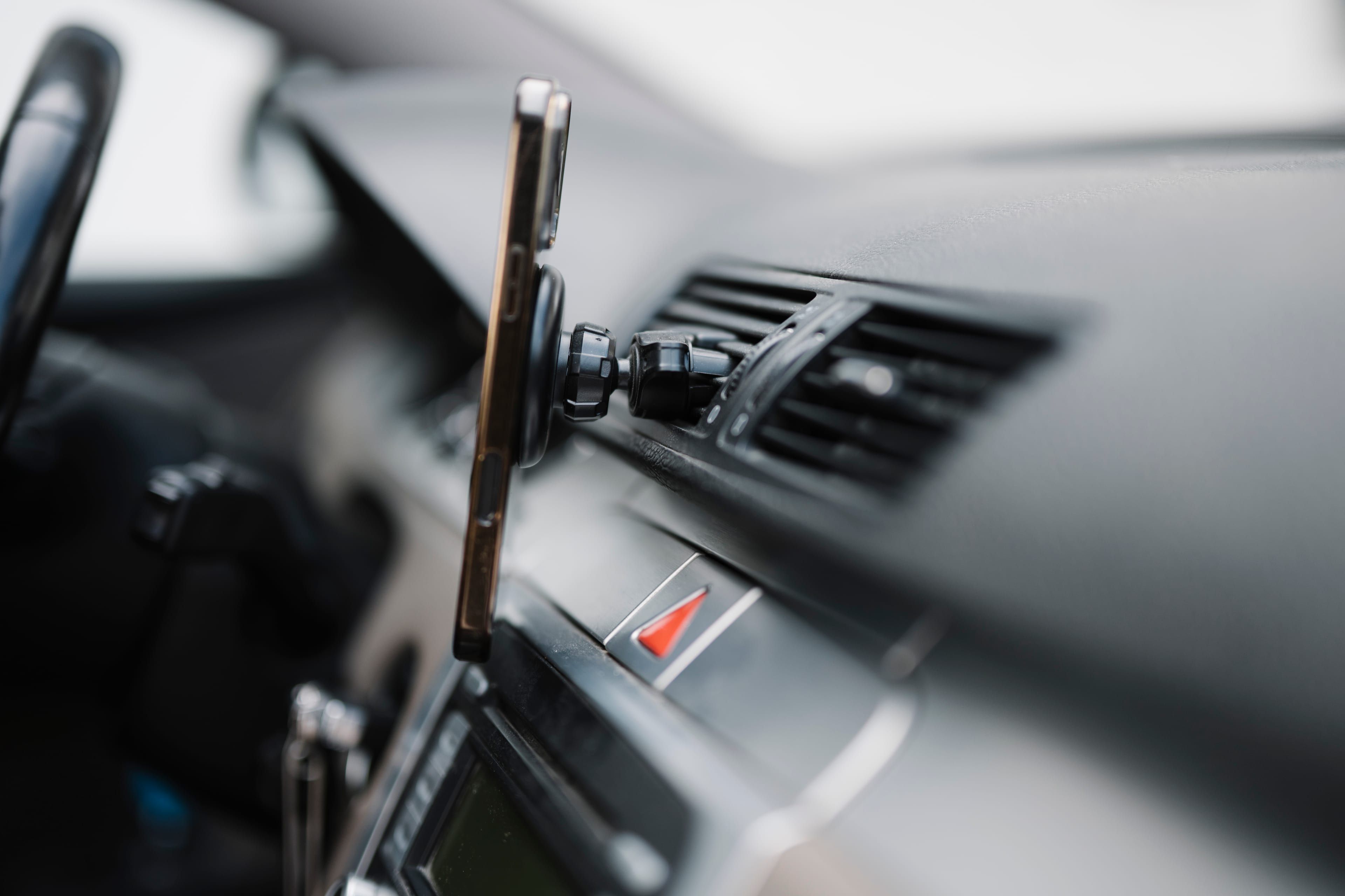 A smartphone held by a magnetic mount on a car's air vent, the dashboard out of focus behind it