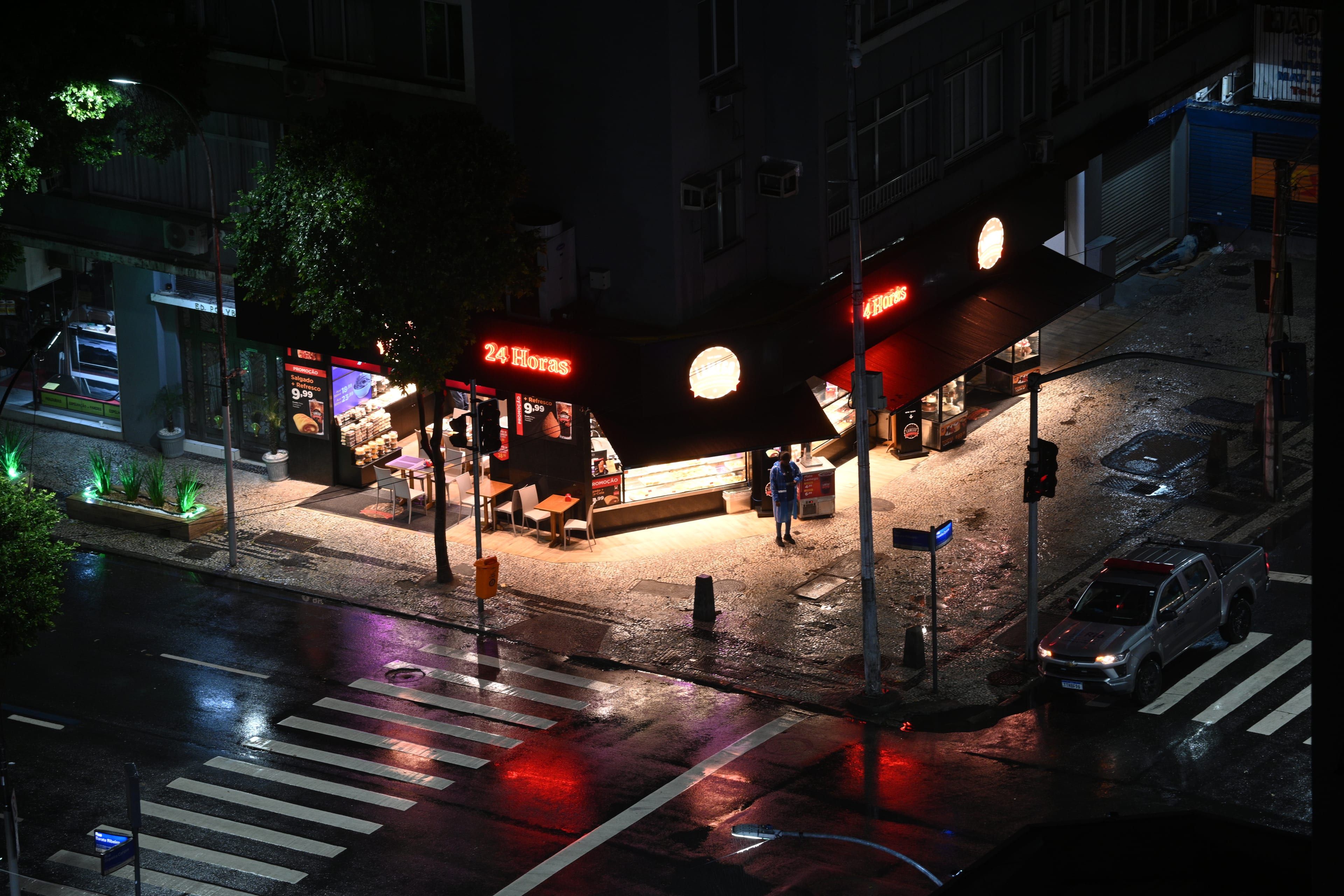 A lit street corner at night after rain, with a pickup truck stopped at the crosswalk.