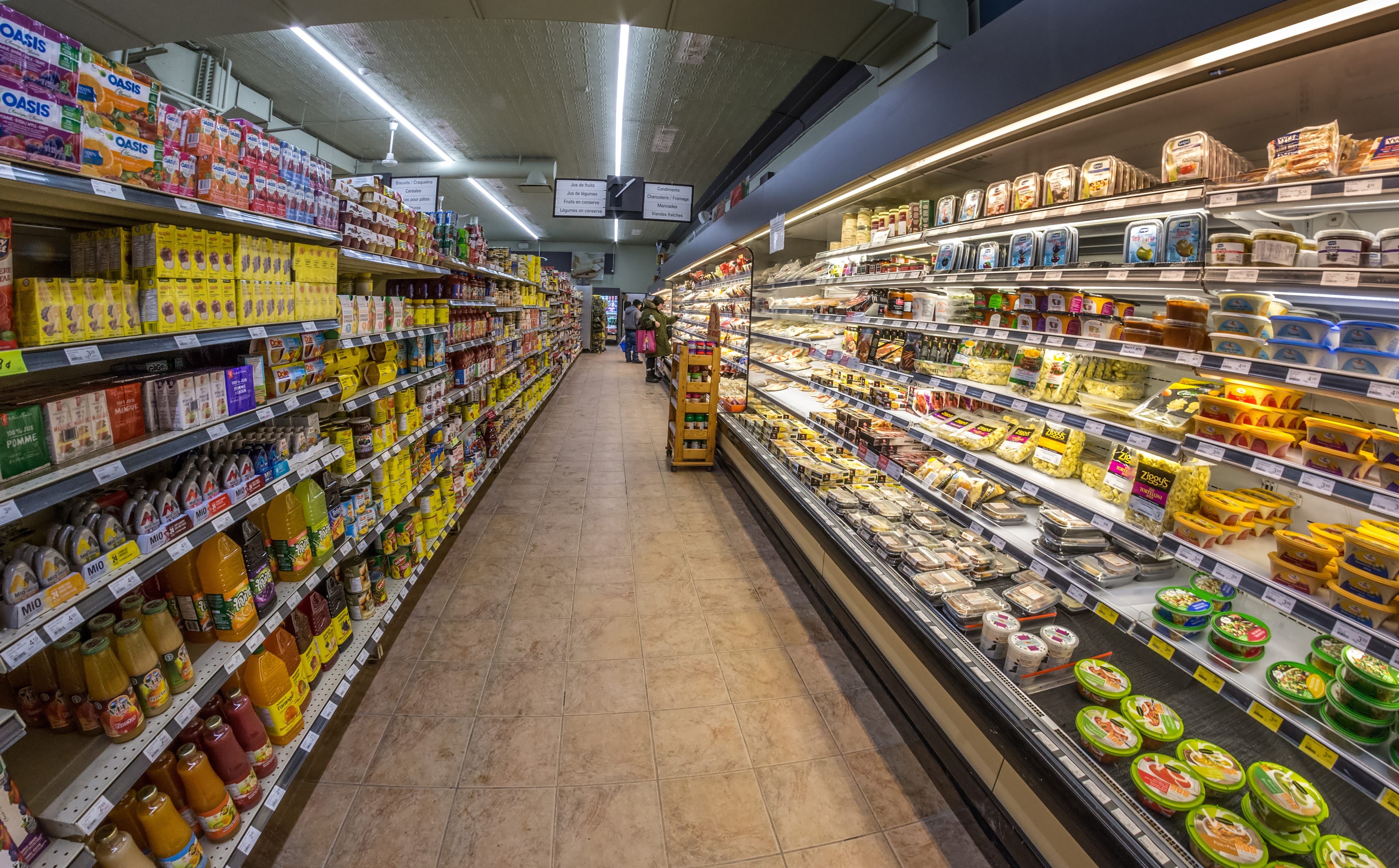 A long supermarket aisle with juice bottles on one side and chilled cases on the other