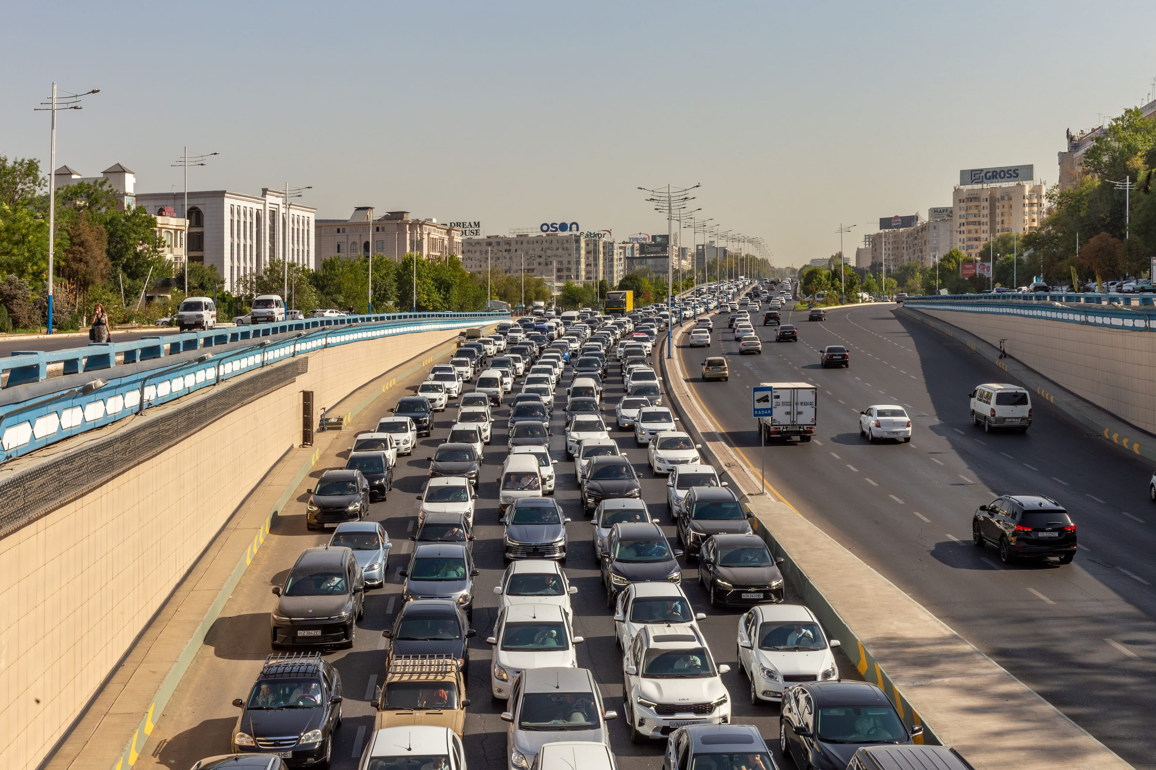 Rows of cars packed onto a wide city road beside an overpass in Tashkent