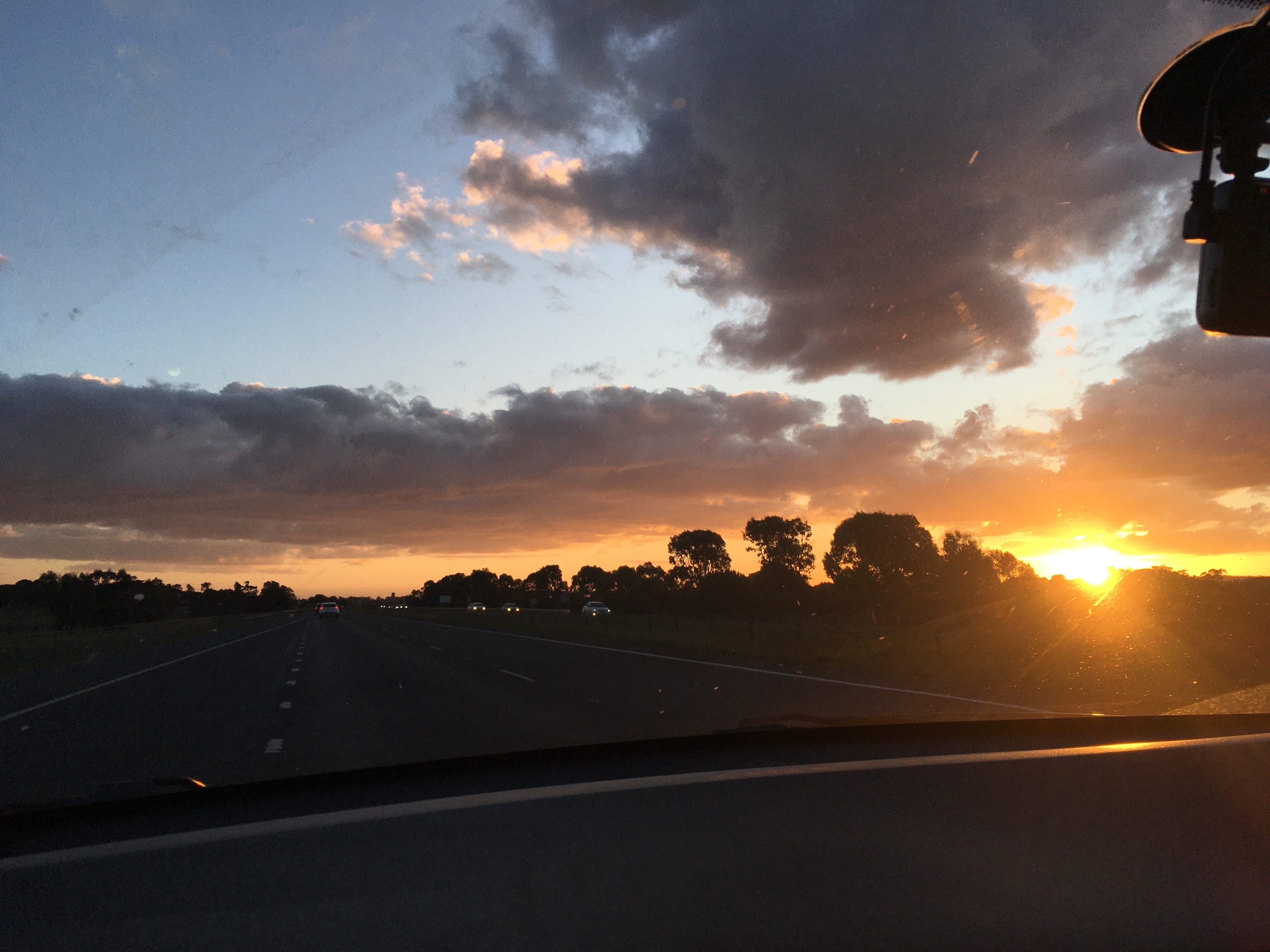 The sun setting over a freeway, seen through a car windshield with a dash camera in the corner